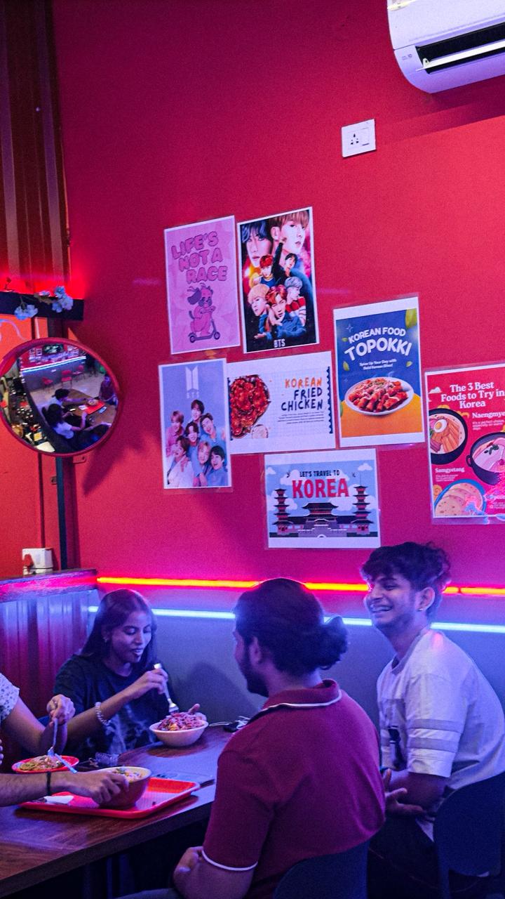 Friends sharing Korean food in the red and blue neon-lit dining area at K-Town Bites